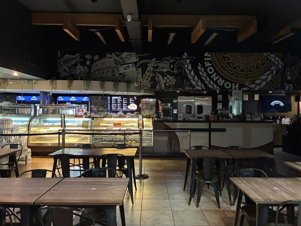 El salón de Apolo: la vitrina de pan encendida, mesas de madera y el mural corriendo bajo las vigas