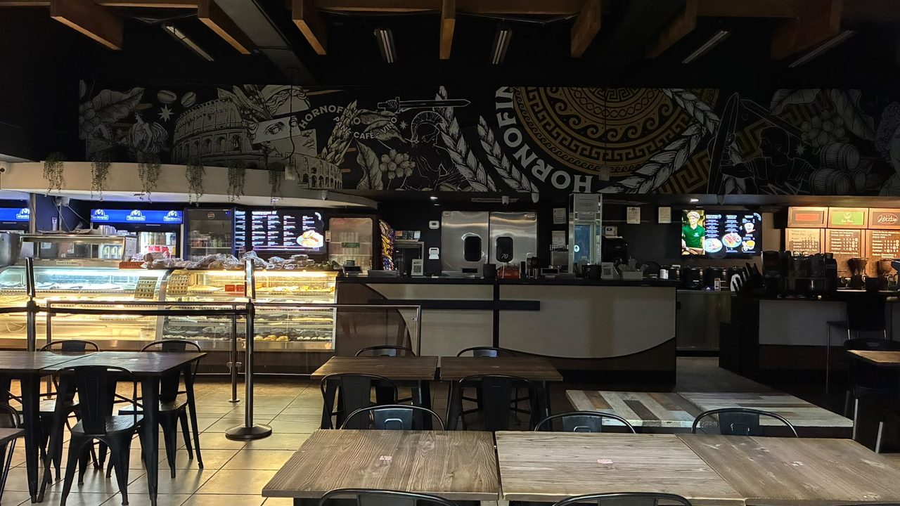 El salón de HORNOFINO Apolo, en Guaynabo: la vitrina de pan encendida, mesas de madera y el mural corriendo por toda la pared bajo las vigas